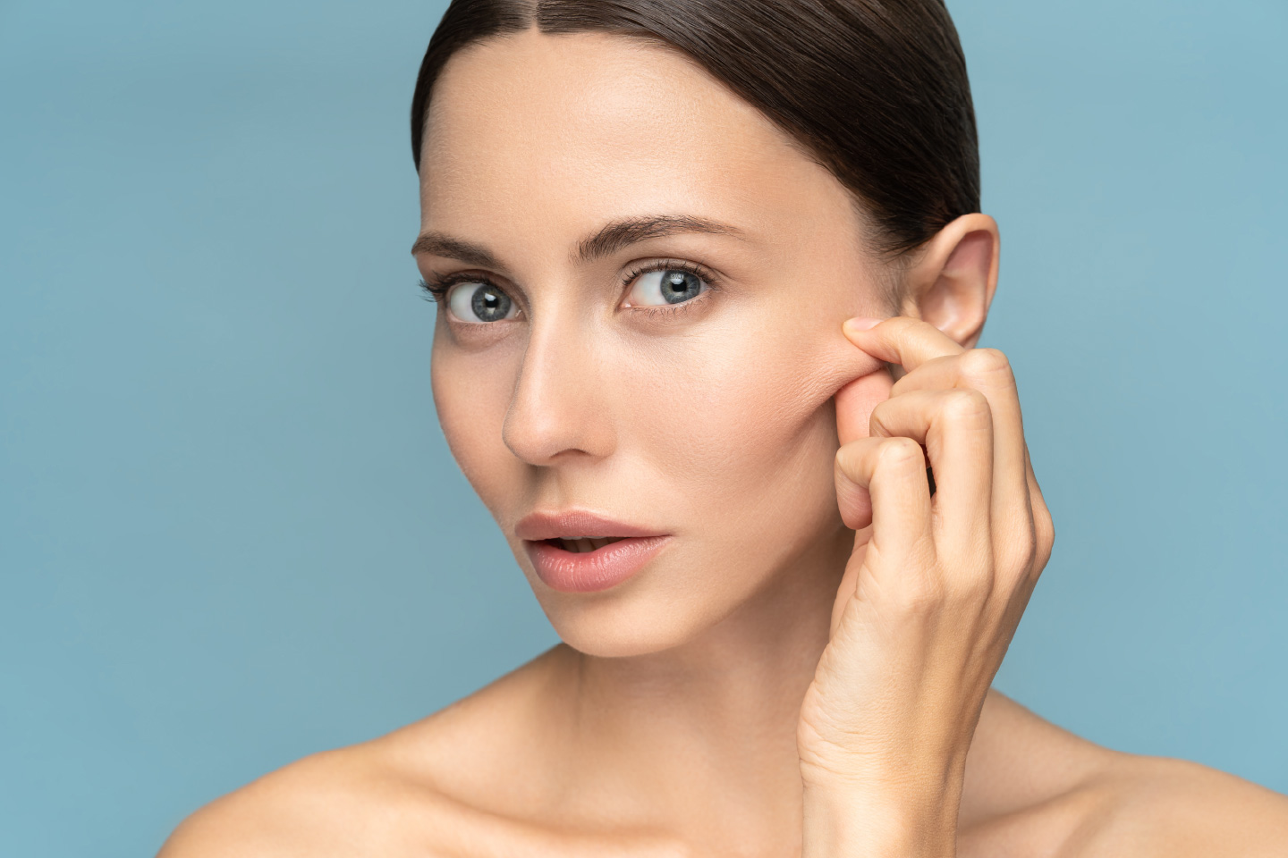 A woman gently pinching the skin near her cheek to show firmness and smooth texture.