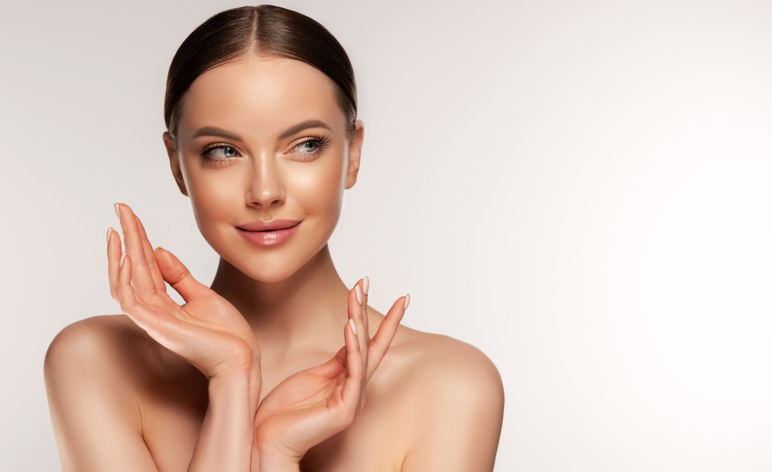 woman with bare shoulders posing with hands raised near her face against a light background