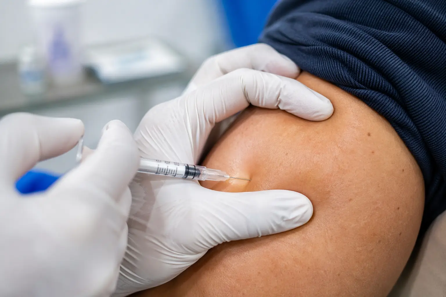 Gloved hands administering injection into upper arm 