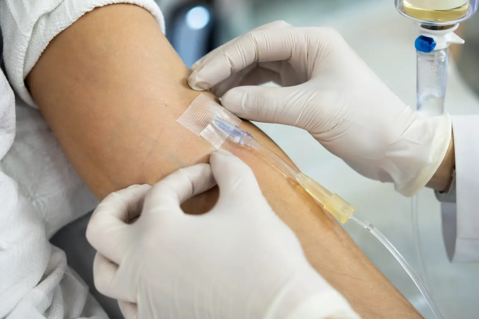 Gloved hands adjusting IV line inserted in patient arm