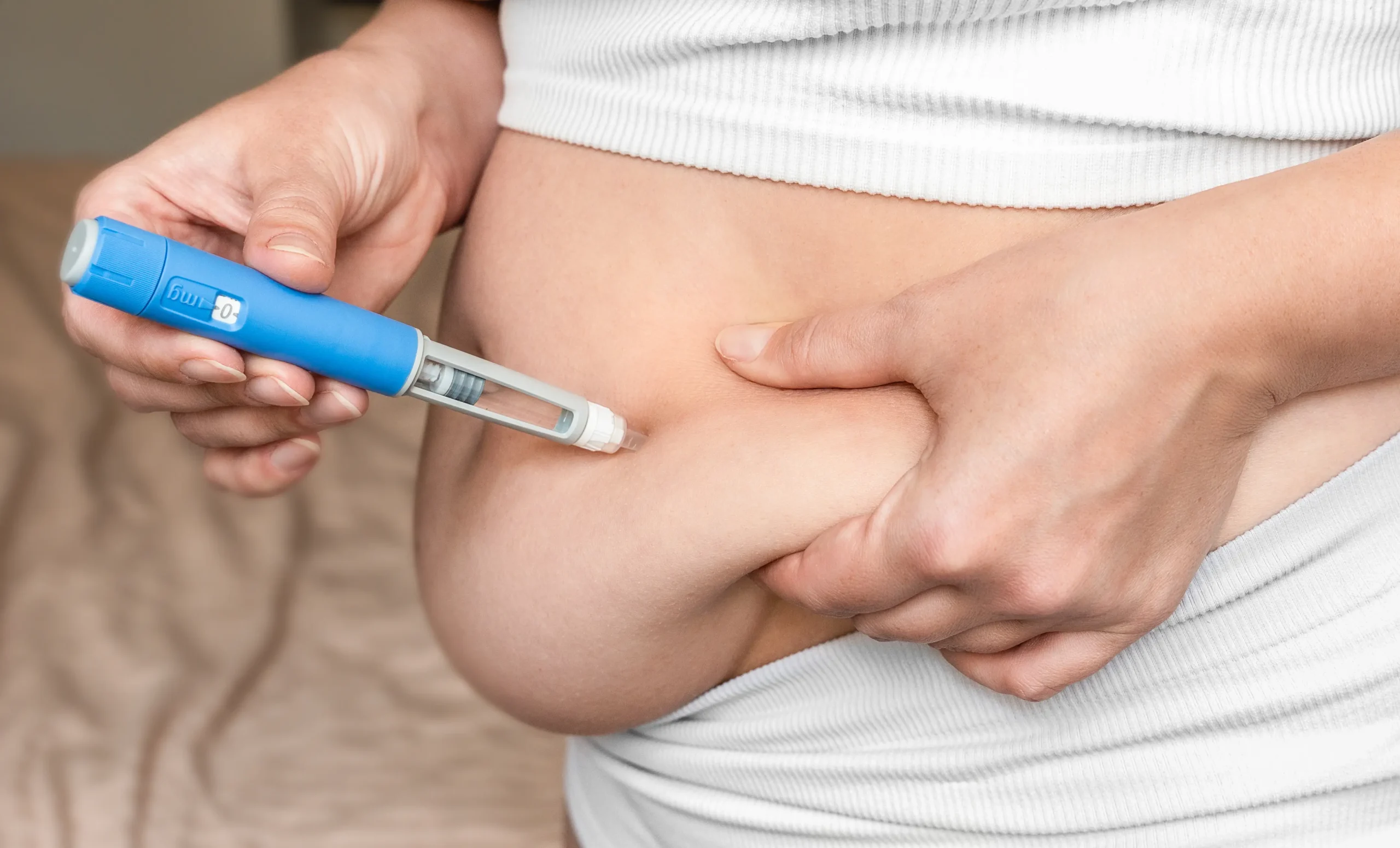 Person administering injection into abdominal area while holding stomach skin 