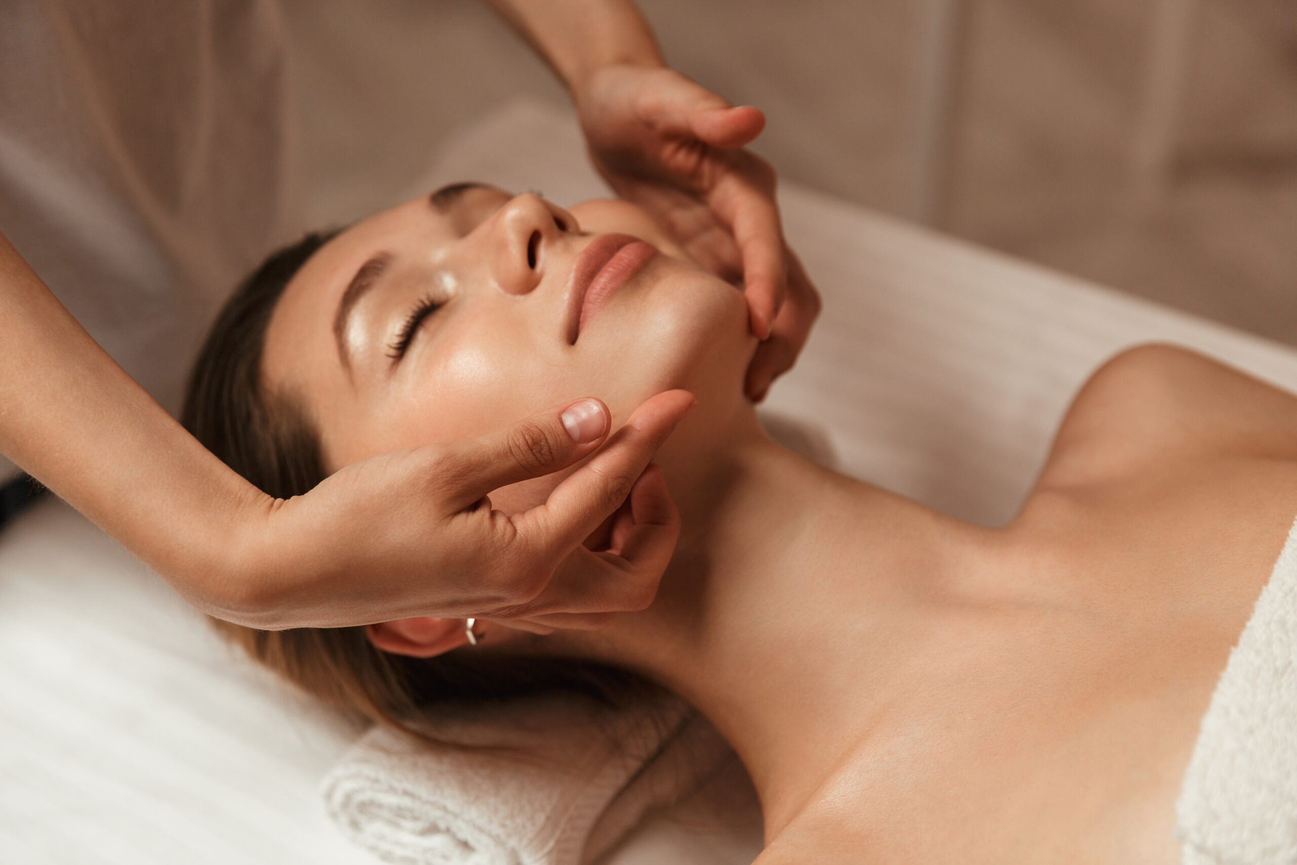 Esthetician performing facial massage on woman lying on spa treatment bed