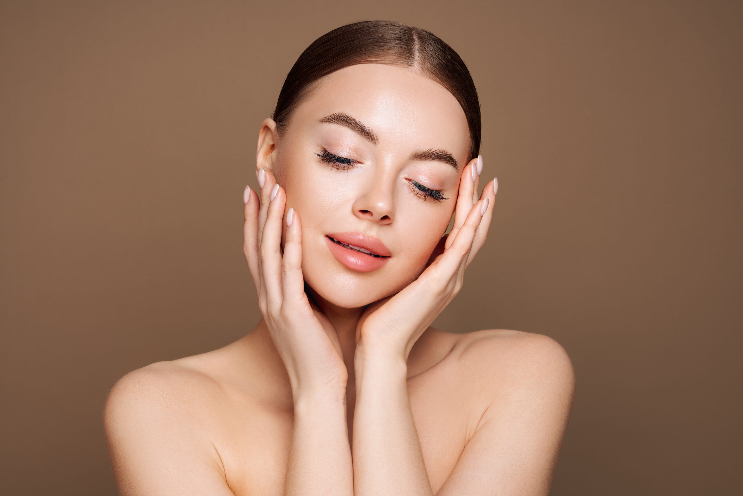 Woman with smooth skin posing with hands on face against neutral background