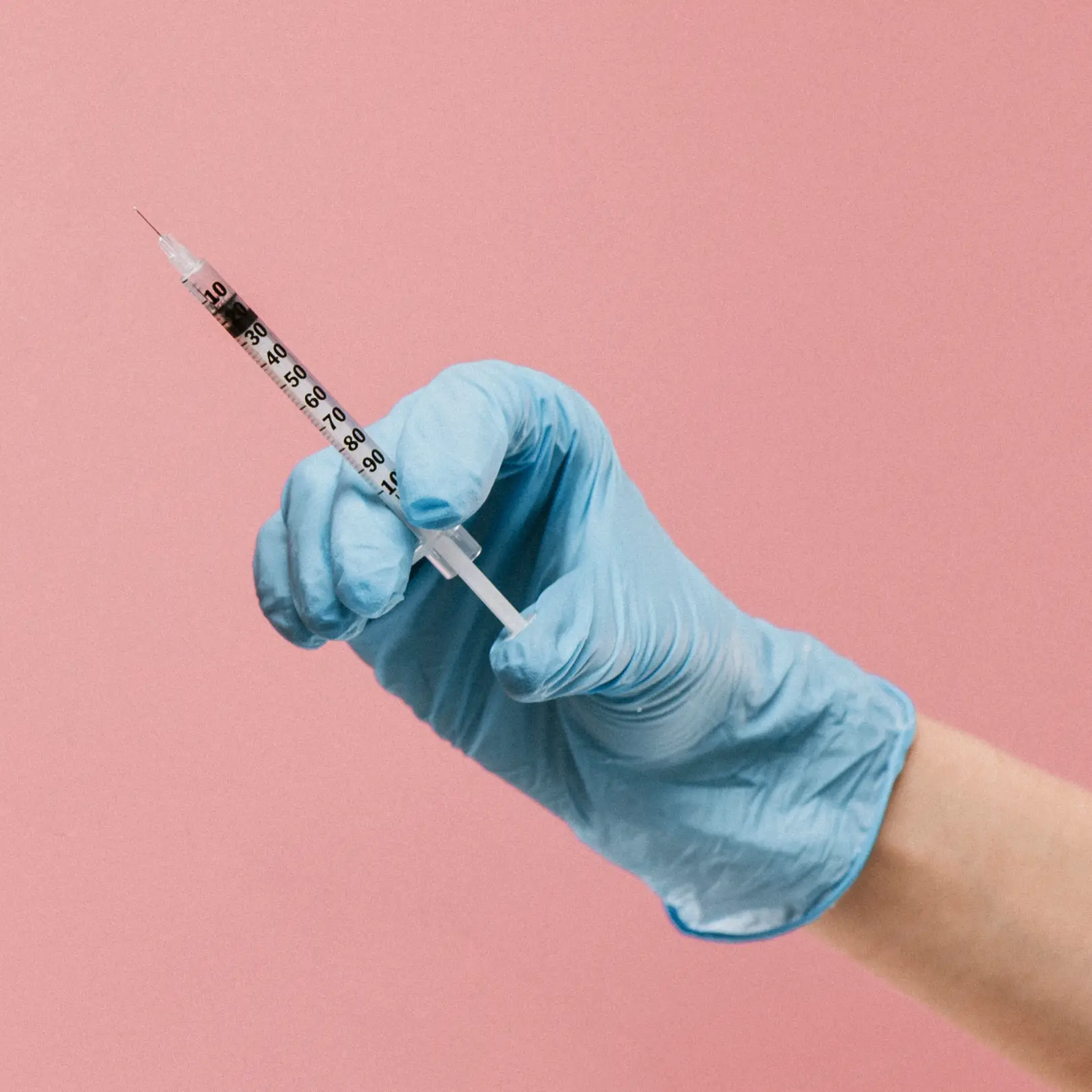 Gloved hand holding a syringe against a pink background.