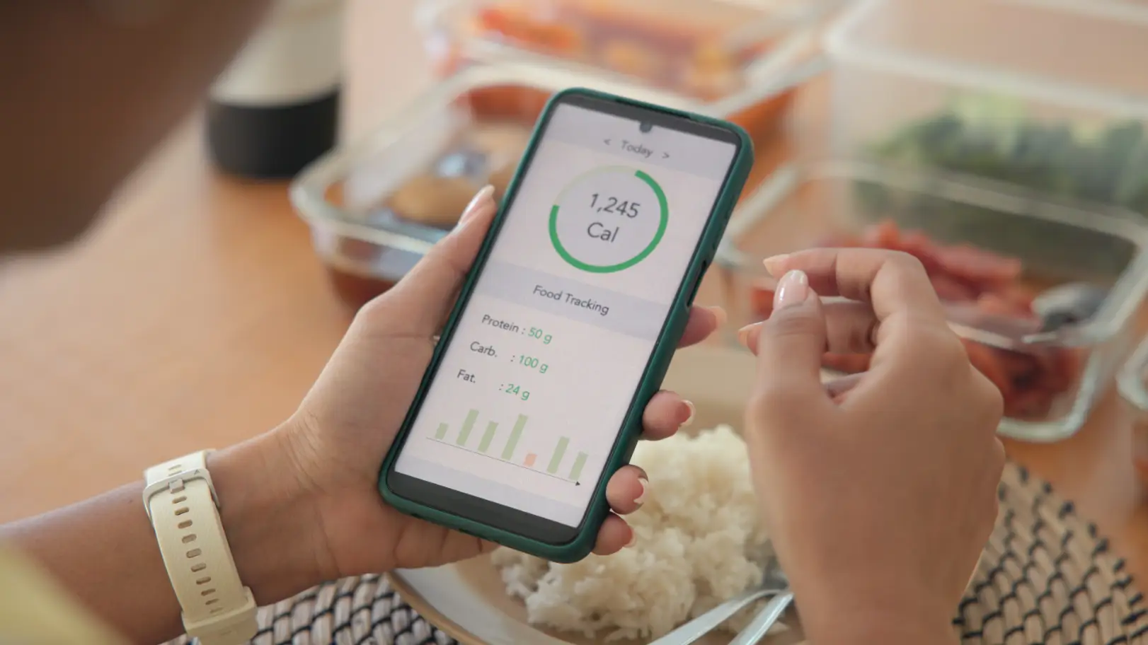 Person holding a smartphone displaying calorie tracking information beside a meal.