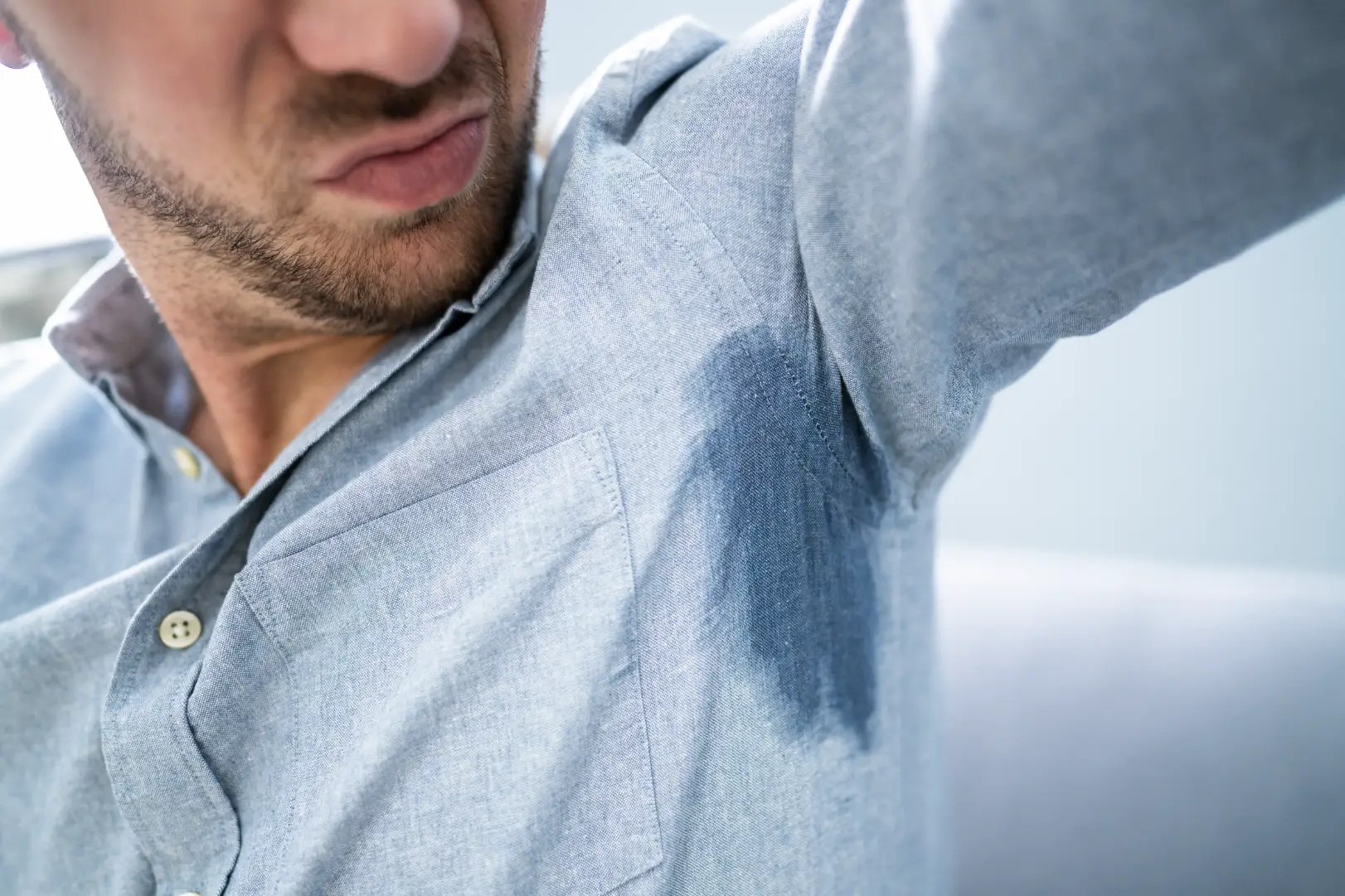 Person looking at a sweat stain under the arm of a light blue shirt.