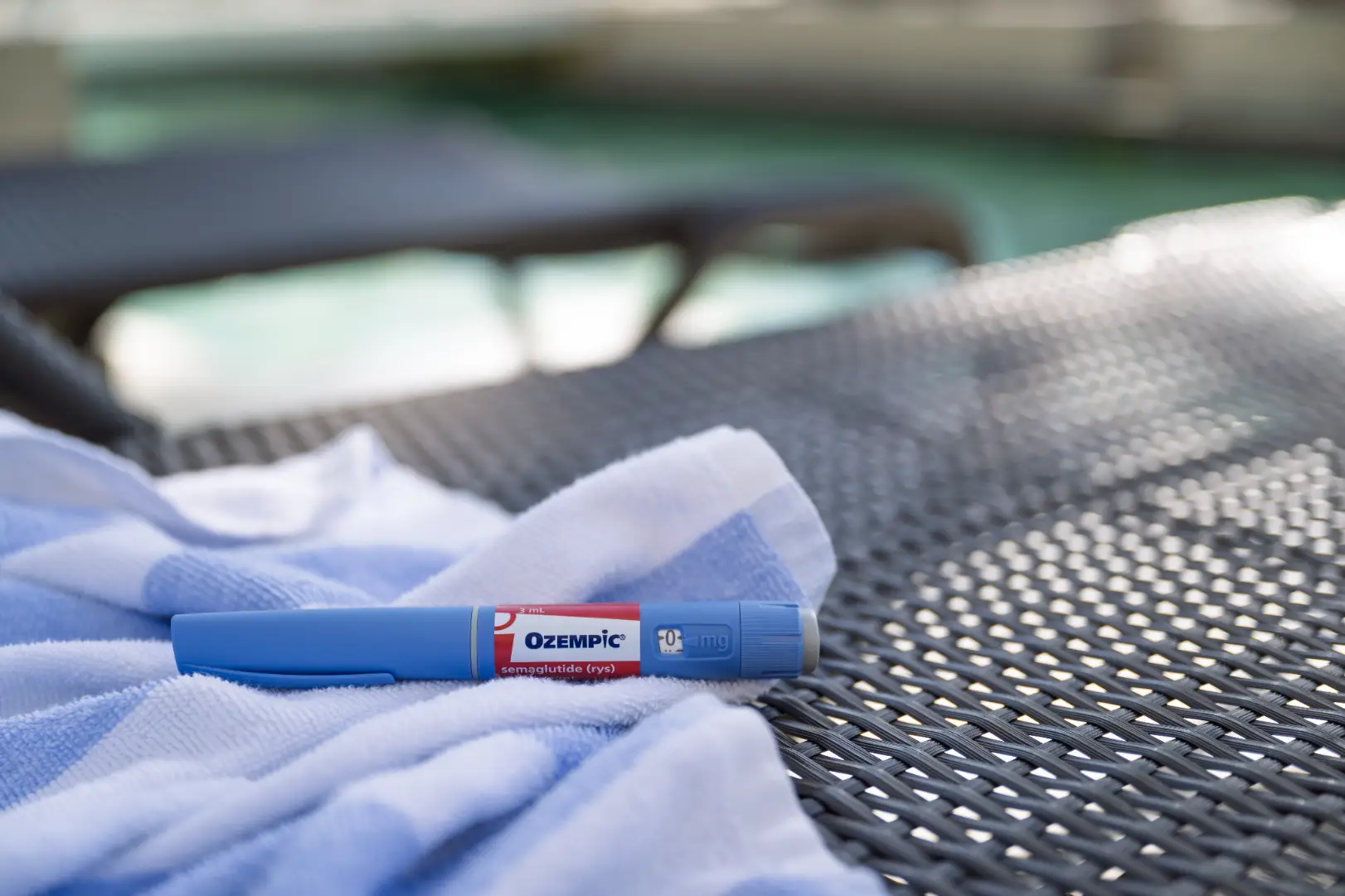 Blue injection pen resting on a towel placed on outdoor woven furniture.